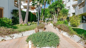 A pathway flanked by white buildings with balconies, palm trees, and a small garden area. - Xabia Port Plus by Interhome (Jávea)