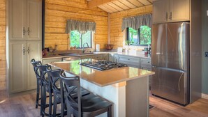 Een moderne keuken met houten wanden, een centraal eiland met barkrukken, roestvrijstalen apparatuur en een raam met uitzicht op groen.