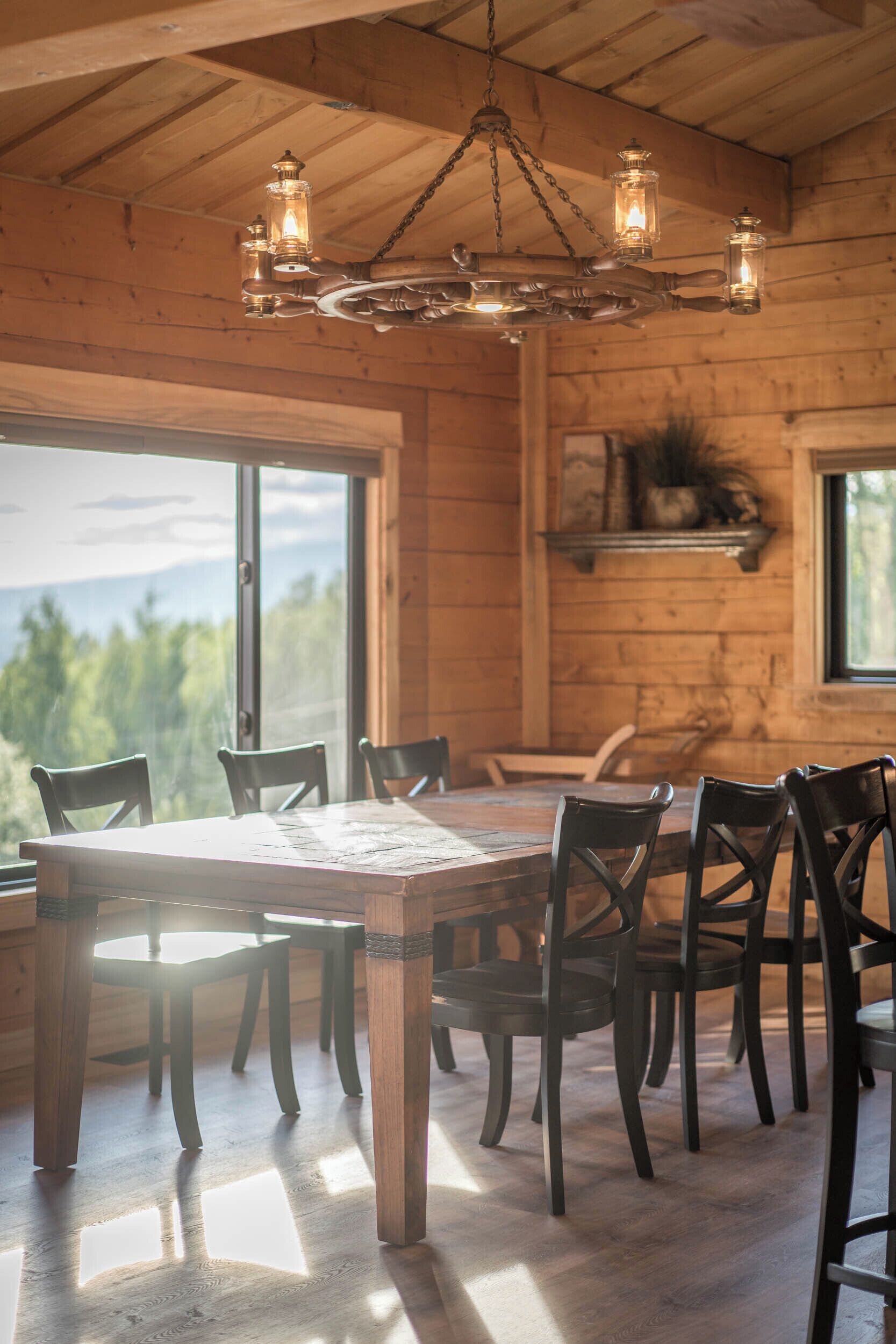 Ein Holzinterieur mit Esstisch und Stühlen, einer Kandelaber und großen Fenstern mit Blick ins Freie.