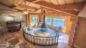 Een gezellig cabin interieur met een centraal gelegen open haard, houten wanden en een groot raam met een prachtig uitzicht.