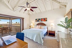 A bedroom with a bed, a desk with a laptop, a ceiling fan, and a view of the outdoors.