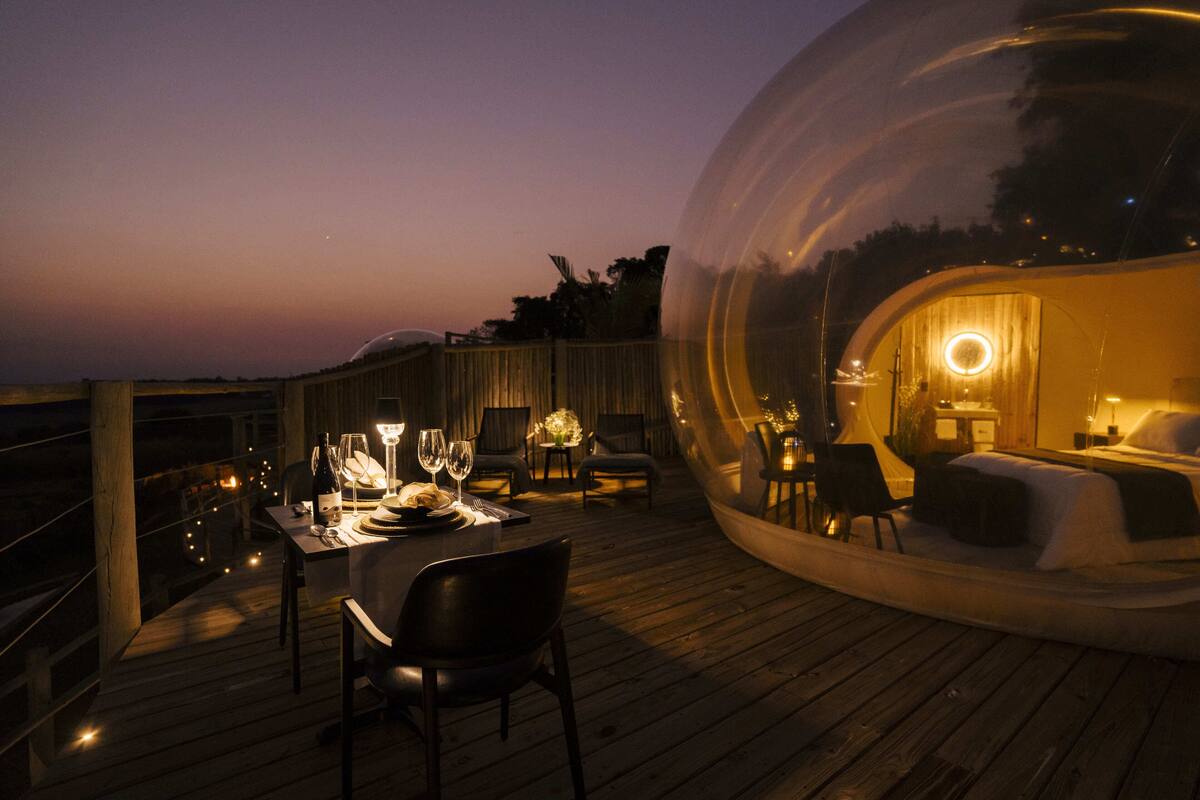 A transparent dome structure with a dining area and a bedroom.