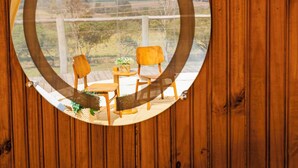 Un mur en bois sur lequel est accroché un miroir rond, reflétant un espace patio avec deux chaises et une table.