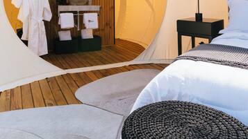 Una habitación tipo tienda de campaña acogedora, con interior de madera, un espejo redondo, un lavamanos y una cama con cabecero.