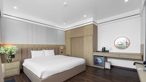 A modern hotel room with a large bed, a wooden wardrobe, a desk with a computer, and a small trash bin. - Pho Co Hotel Ninh Binh (Ninh Binh)
