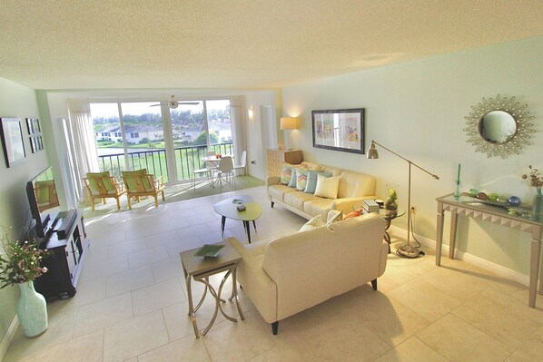 A spacious living room with a sofa, a coffee table, and a balcony with a view of the outdoors.