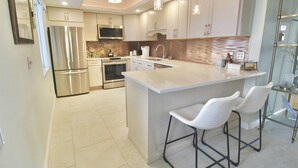 A modern kitchen with stainless steel appliances, a large island with bar stools, and a tiled backsplash. - Catamaran - Beautifully Renovated 2 BR Condo - Golf Course Enclosed Balcony View - Oceanfront Resort (Fort Pierce)