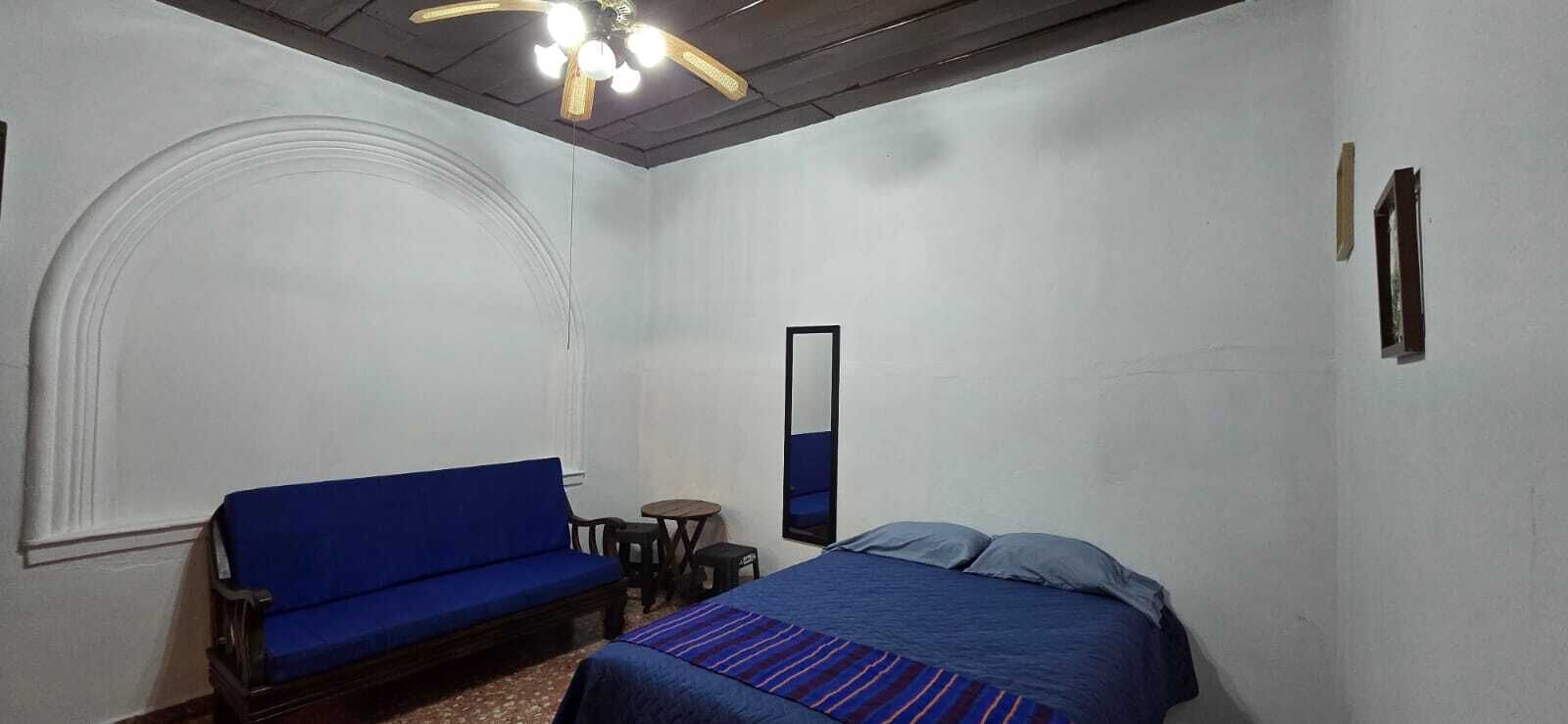 A room with a bed, a blue sofa, a small table, and a ceiling fan.