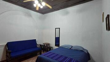A room with a bed, a blue sofa, a small table, and a ceiling fan.