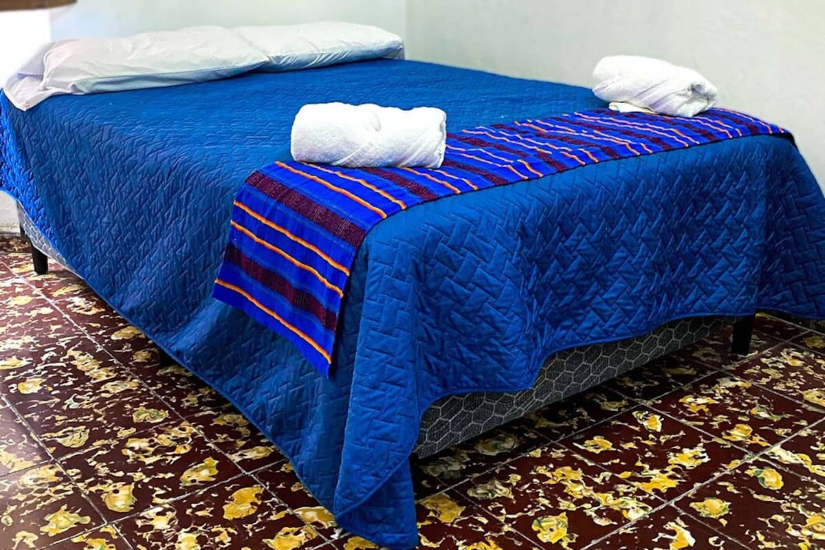 Un lit simple avec une couette bleue et une couverture à rayures, des oreillers blancs et une serviette pliée posée sur le lit.