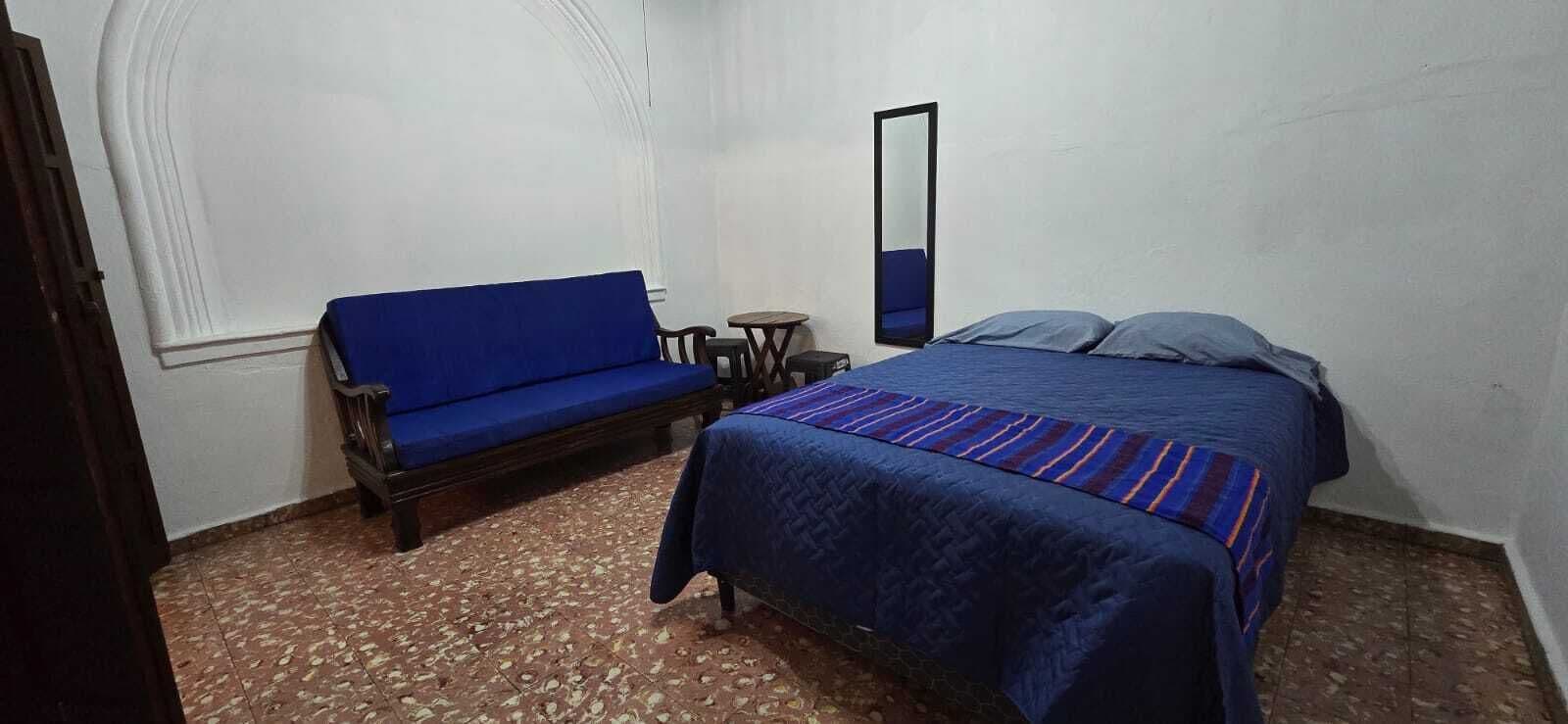 Een slaapkamer met een bed, een blauwe bank, een klein tafeltje en een spiegel.