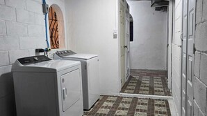 Ein Waschraum mit zwei Waschmaschinen und einem Trockner, einem Fliesenboden und einer Tür zu einem anderen Raum.