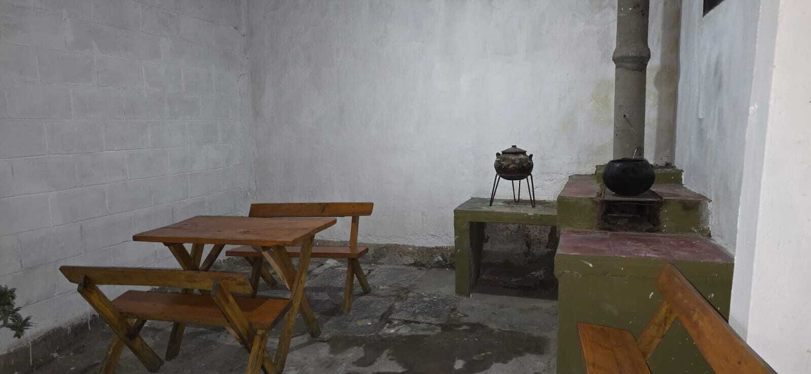 Un piccolo ambiente chiuso con un tavolo e panche di legno, uno sgabello e un tradizionale stufa.