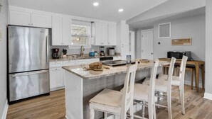Una cocina moderna con armarios blancos, un refrigerador de acero inoxidable, una isla integrada con asientos y un microondas.
