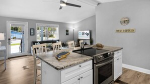 Una cocina moderna con horno empotrado, comedor con mesa y sillas blancas, y ventilador de techo.