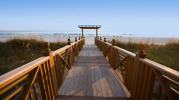 Una pasarela de madera que conduce a una playa, con un porche de madera al final.
