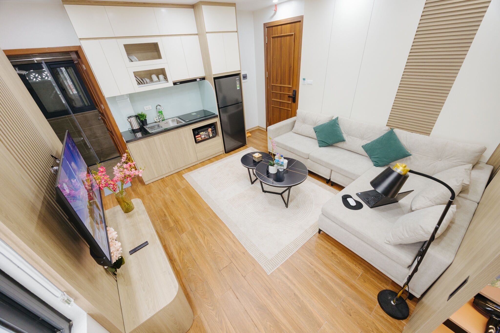 A compact living space with a kitchenette, a sofa with cushions, a coffee table, a TV, and a decorative vase with flowers.