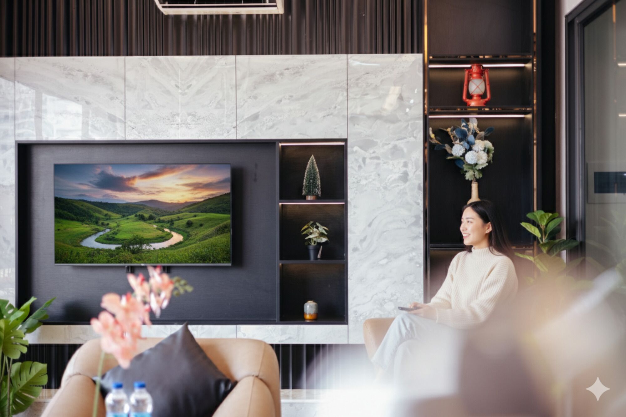 A modern living room with a flat-screen TV mounted on a marble wall, a sofa, and a decorative shelf with plants and a lantern.