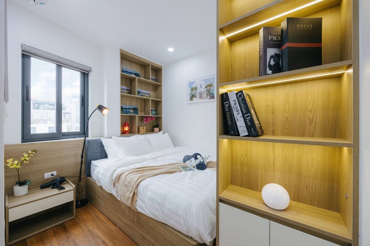 Ein modernes Schlafzimmer mit Bett, Nachttisch, Lampe und eingebauten Holzbögen mit Büchern und einer Vase.