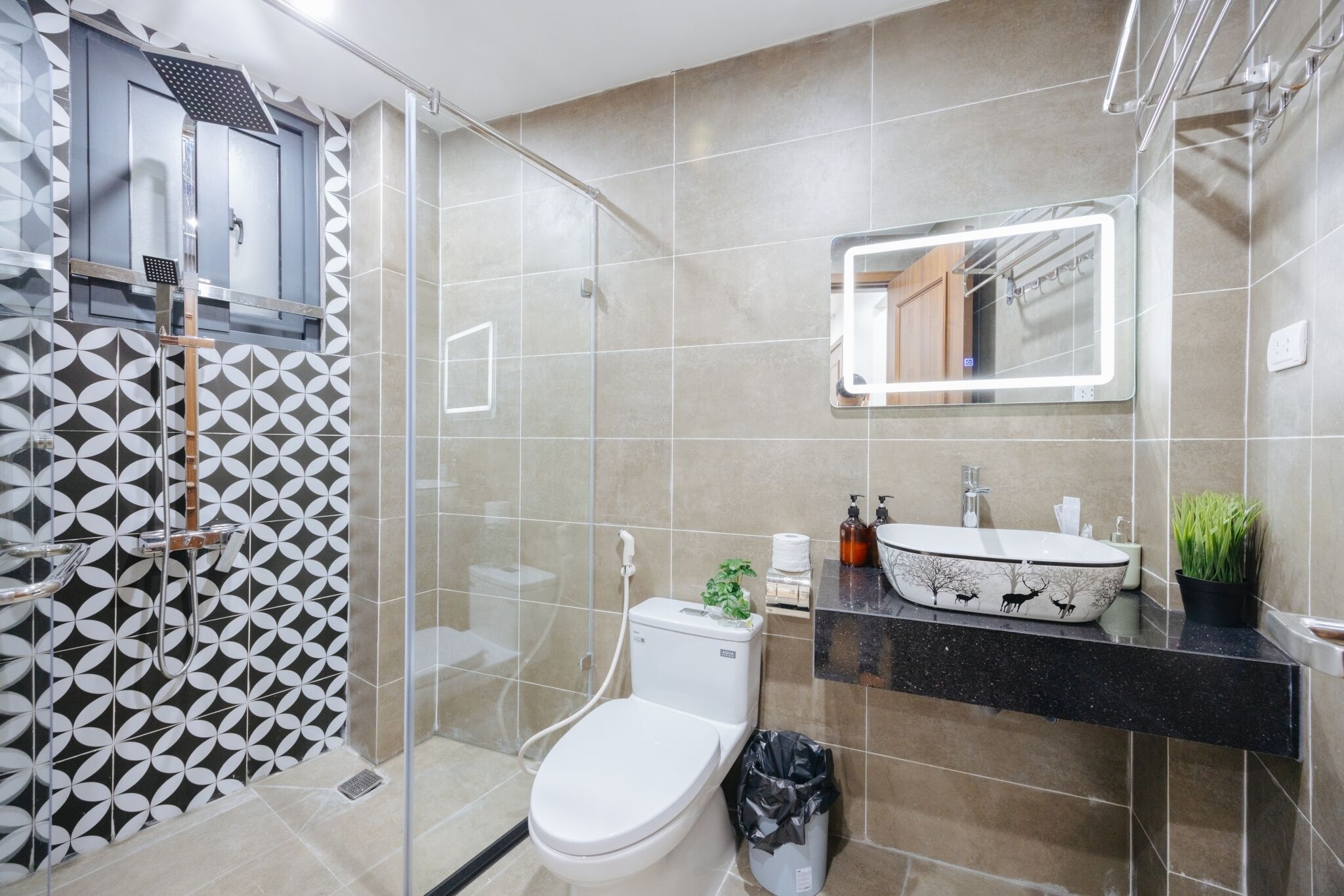 A modern bathroom with a glass shower enclosure, a toilet, a sink with a decorative basin, and a mirror with integrated lighting.