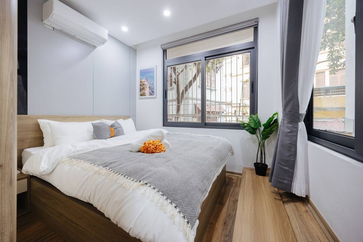 Ein Schlafzimmer mit einem hölzernen Bett, weißer Bettwäsche, einem Fenster mit Ausblick und einer Topfpflanze.