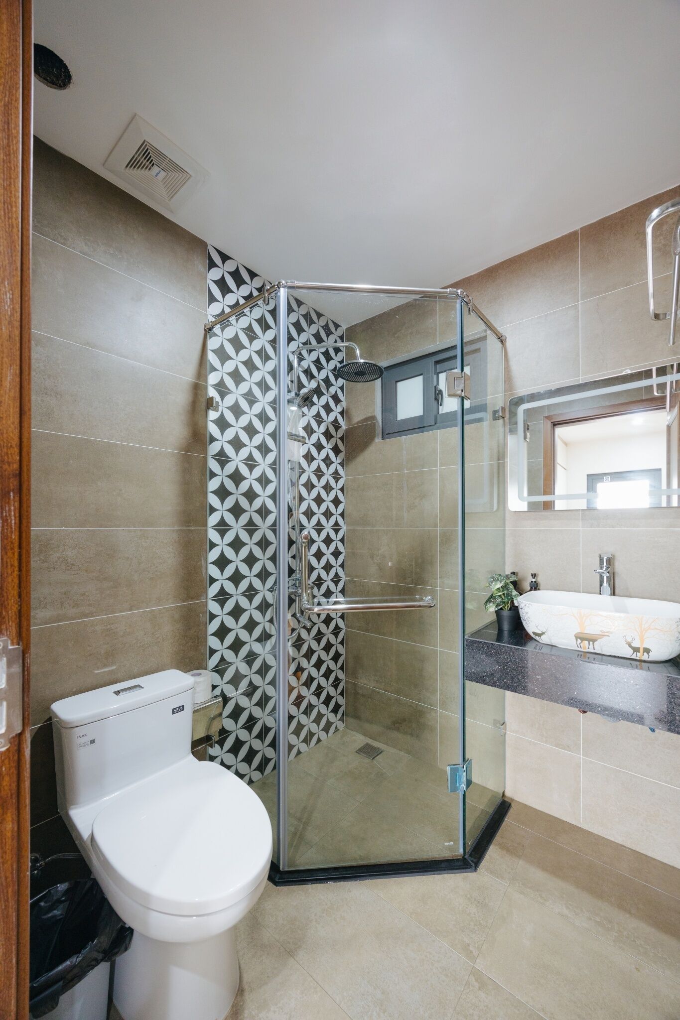 A modern bathroom with a glass-enclosed shower, a white toilet, and a sink with a decorative mirror.