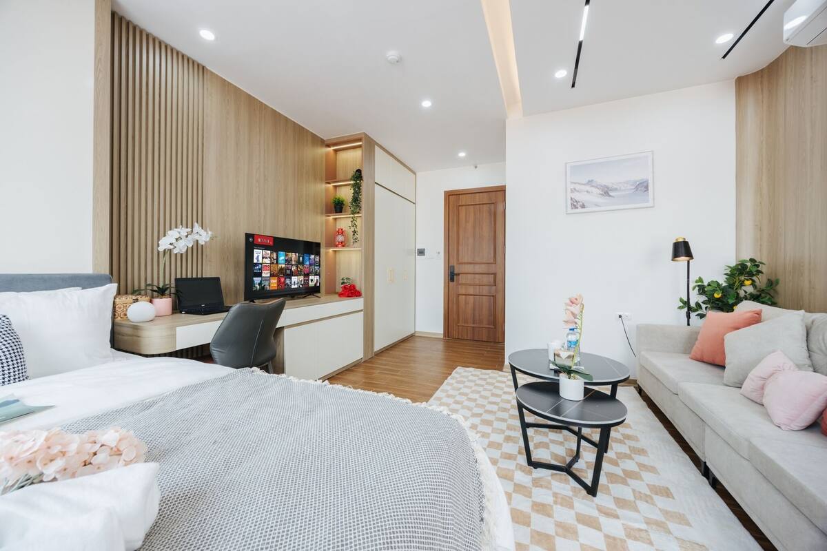 Ein modernes Hotelzimmer mit einem Bett, einem Schreibtisch mit Computer, einer Couch und einem kleinen Tisch mit Pflanze.