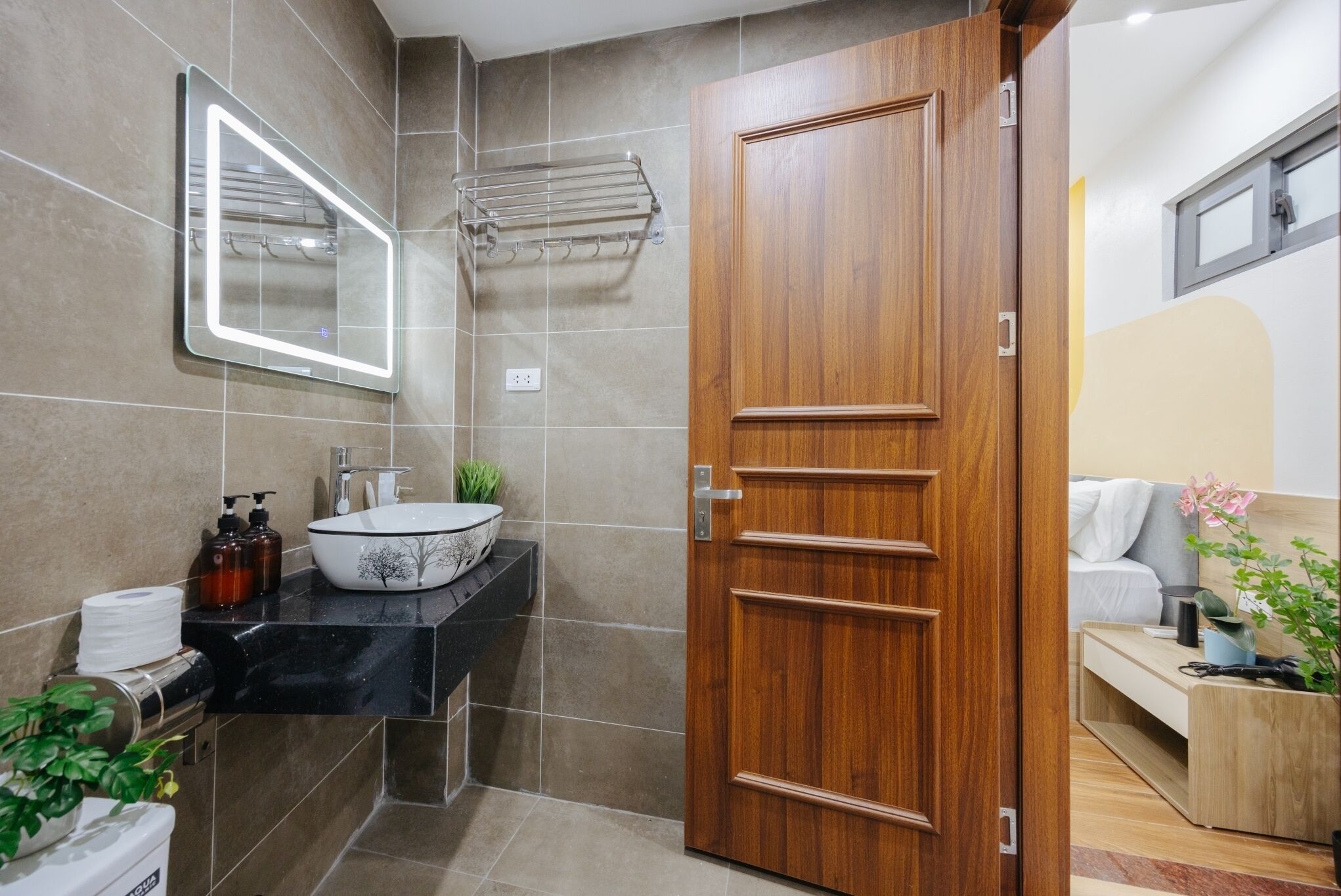 Ein modernes Badezimmer mit Holztür, schwarzer Waschtischplatte, weißem Waschbecken und einem Spiegel.