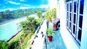 Un balcon donnant sur une rivière et sur la verdure, avec une plante en pot et une chaise.