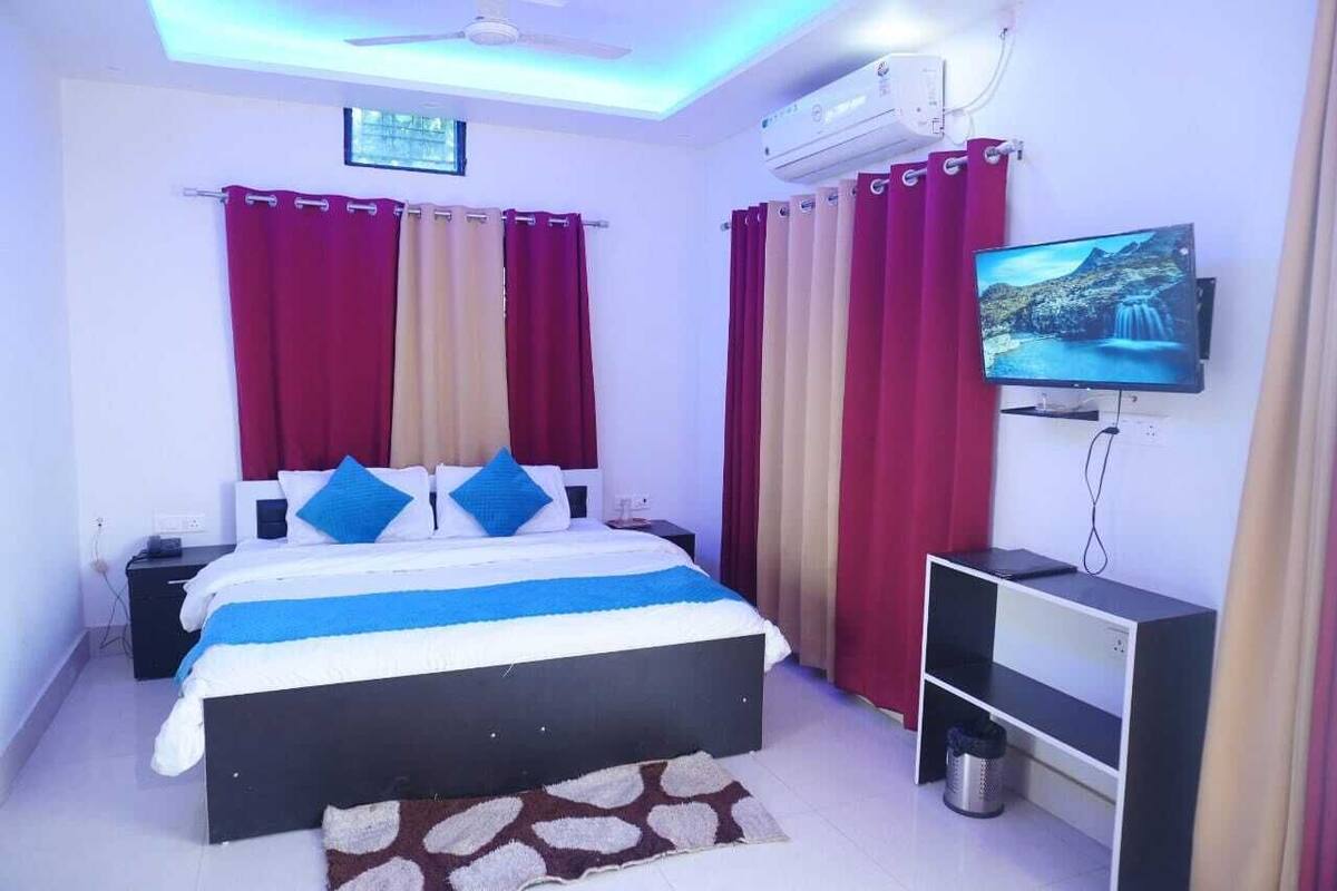 A bedroom with a bed, curtains, a TV, and a ceiling fan.