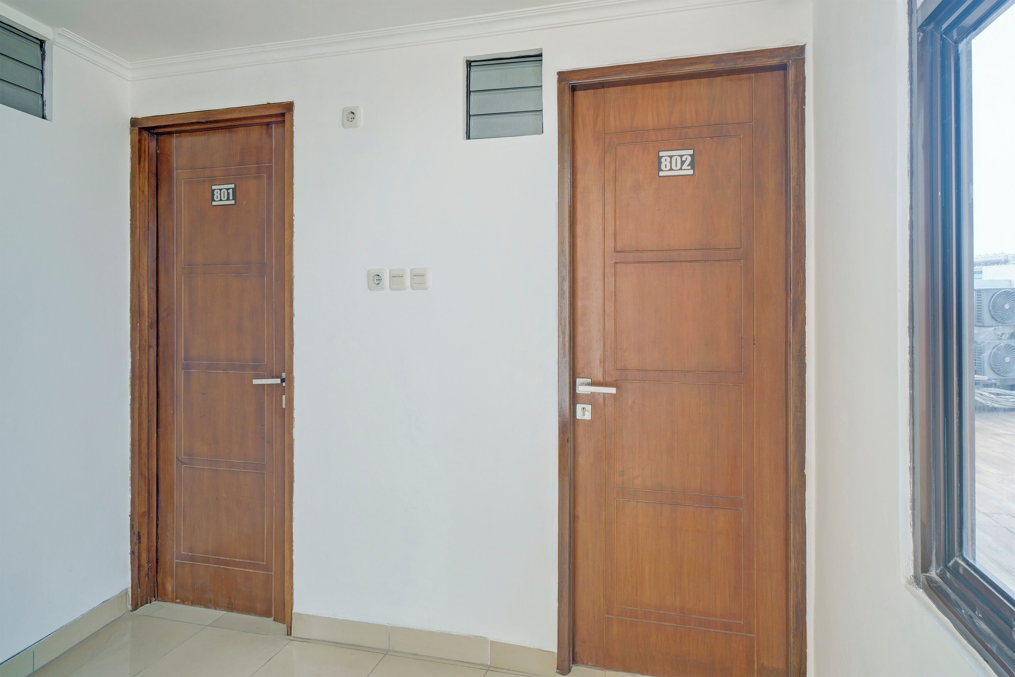 Two wooden doors with numbers 801 and 802, a small window with a view of a building, and a tiled floor.