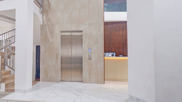 A modern elevator in a lobby with a marble floor, a staircase to the left, and a reception desk with a wooden panel backdrop. - Townhouse Oak Ancol (Jakarta)