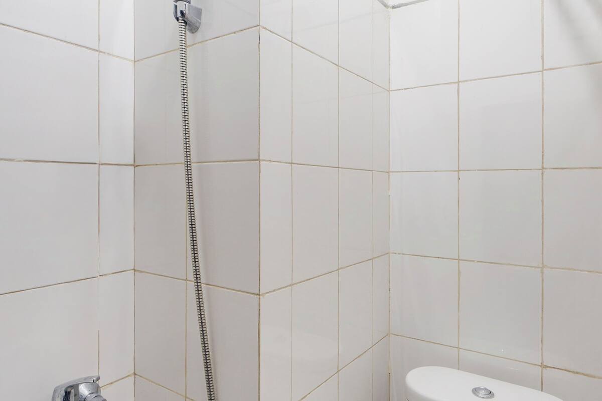 A bathroom with white tiles, a shower with a handheld showerhead, and a toilet.