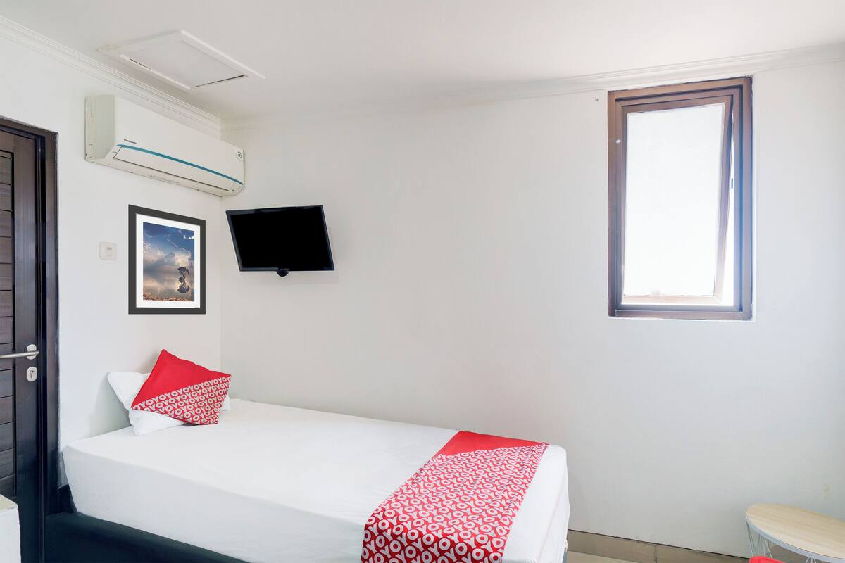 A hotel room with a bed, a TV mounted on the wall, a window, and an air conditioning unit.