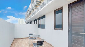 A balcony with a table and chairs, a view of a high-rise building, and a closed sliding door. - Townhouse Oak Ancol (Jakarta)