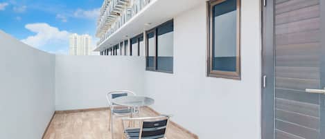 A balcony with a table and chairs, a view of a high-rise building, and a closed sliding door.
