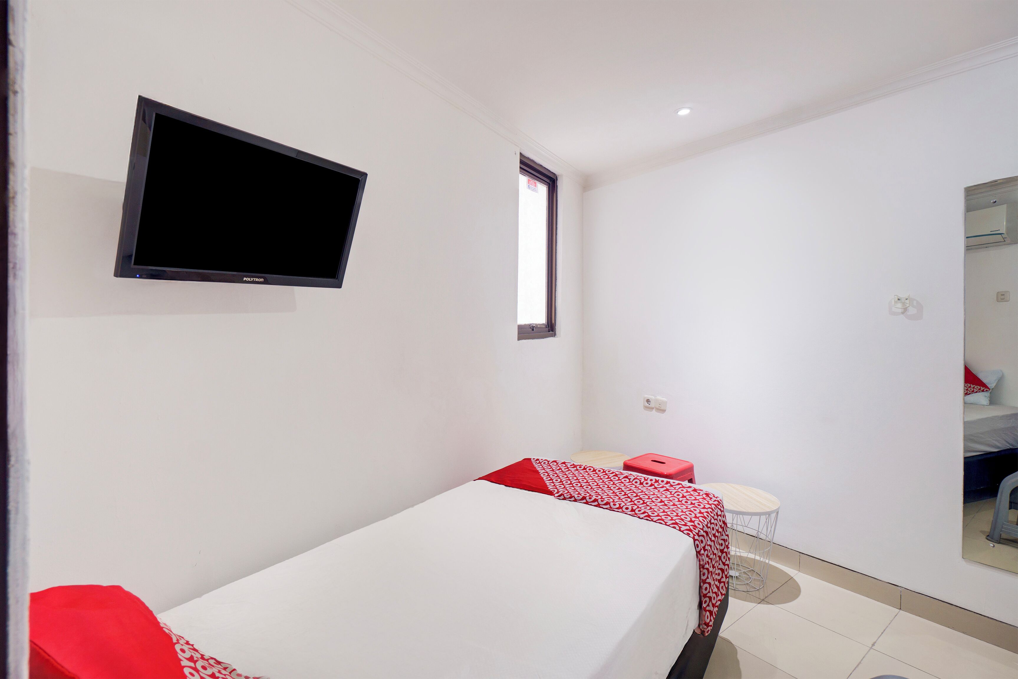 Quarto pequeno e limpo com uma cama, televisão na parede, uma mesinha e uma janela.