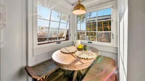 A sunroom with a wooden table and bench, large windows, and a hanging light fixture.