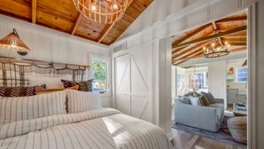 A spacious bedroom with a large bed, a wooden ceiling, and a view into another room with a sofa.