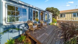 A single-story house with a wooden deck, two chairs, and a table.