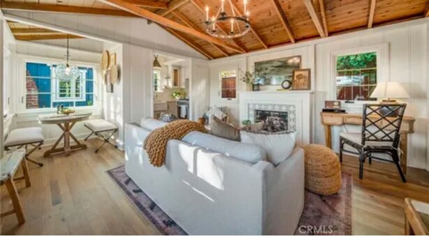 A spacious living room with a white sofa, wooden ceiling beams, a chandelier, and a fireplace.