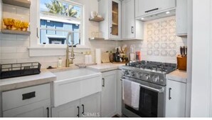 A kitchen with white cabinets, a gas stove, and a window with a view of palm trees.