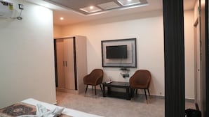 A hotel room with a bed, a desk with two chairs, a television, and a wardrobe. - Hotel Banaras Palace (Varanasi)