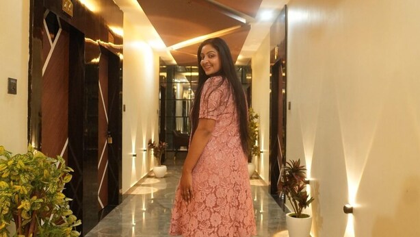 A woman in a pink dress walking down a hallway with marble floors, potted plants, and modern lighting fixtures. - Hotel Banaras Palace (Varanasi)