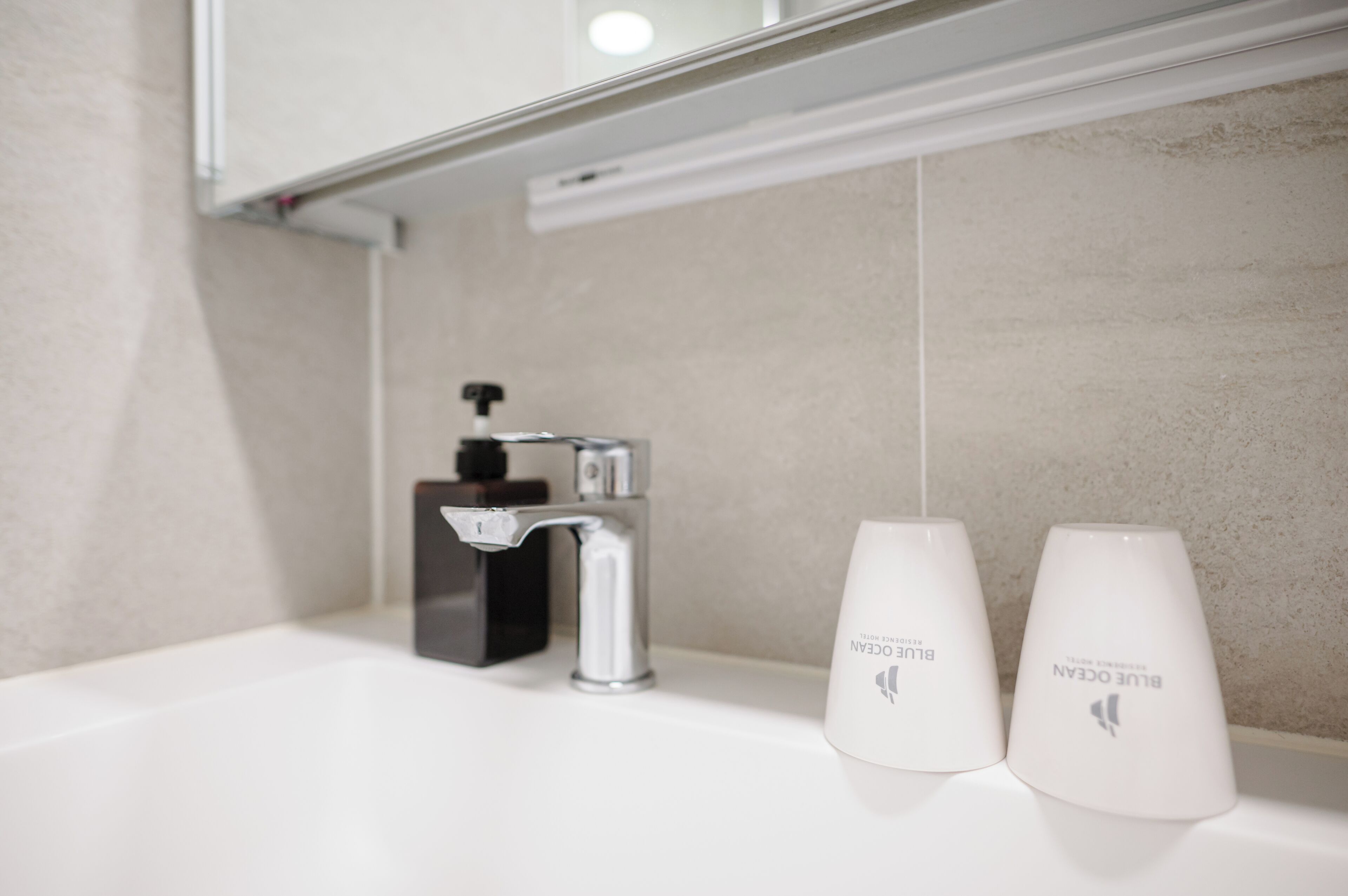 Un baño con un lavamanos blanco, un grifo moderno y dos tazas blancas con el logotipo de Blue Ocean.