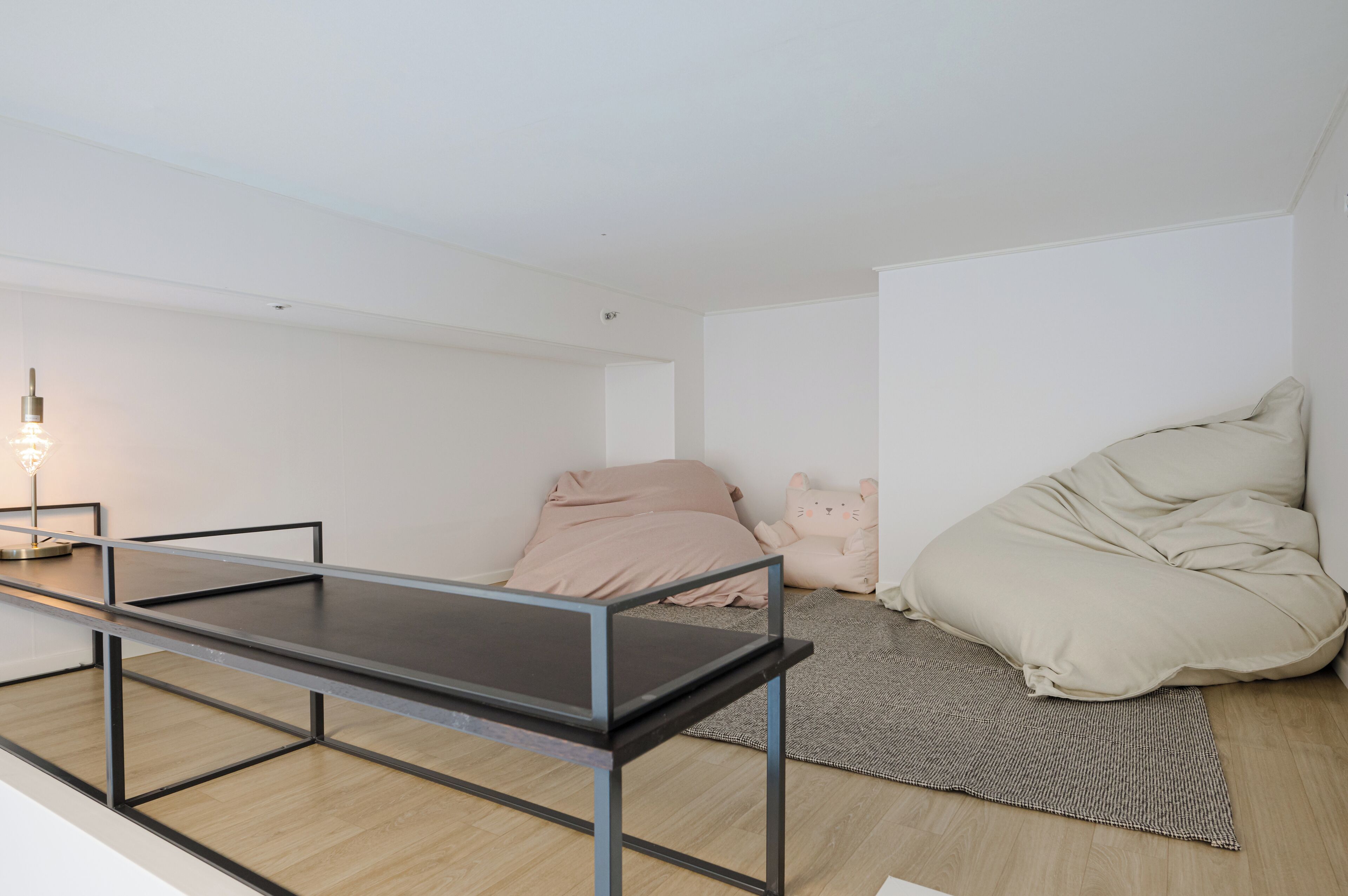 A minimalist room with a metal-framed table, a bed with a beige blanket, and a small lamp.
