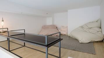 A minimalist room with a metal-framed table, a bed with a beige blanket, and a small lamp.