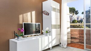 Ein modernes Wohnzimmer mit einem Flachbildfernseher auf einer weißen Konsole, einer Topfpflanze und einem dekorativen Gegenstand an der Wand.