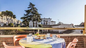 Eine Terrasse mit Tisch für zwei Personen, ausgestattet mit Tischdecke, Stühlen und einem kleinen Tisch mit Kuchen und Gebäck.