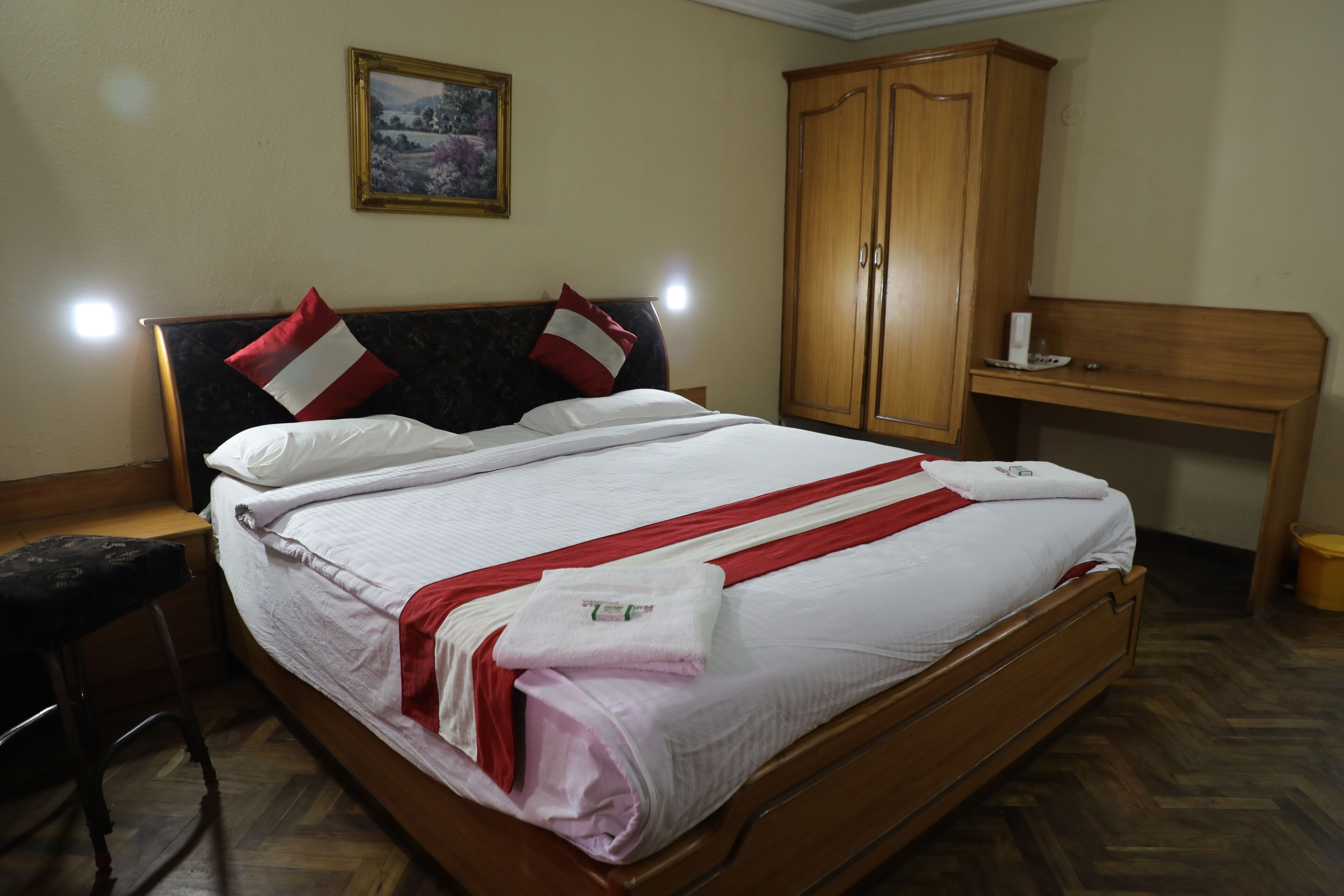 A neatly made bed with a red and white striped blanket, a wooden headboard, and a wooden wardrobe in a hotel room.